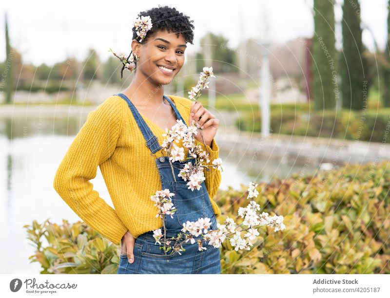 Tender black woman with blooming branches in park spring flower cheerful tender season smile female ethnic african american nature glad charming lake pond