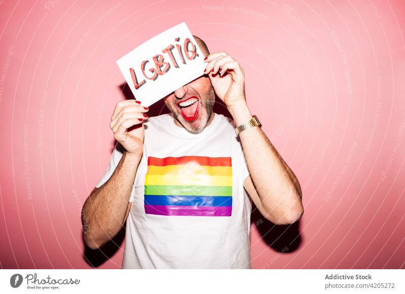 Positive gay showing paper with LGBTIQ inscription in pink studio man homosexual lgbtiq pride queer grimace concept demonstrate hide support cover face activism