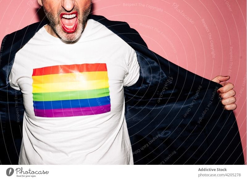 Anonymous excited gay showing t shirt with rainbow flag against pink background man lgbt homosexual queer demonstrate concept tolerance equal liberty respect