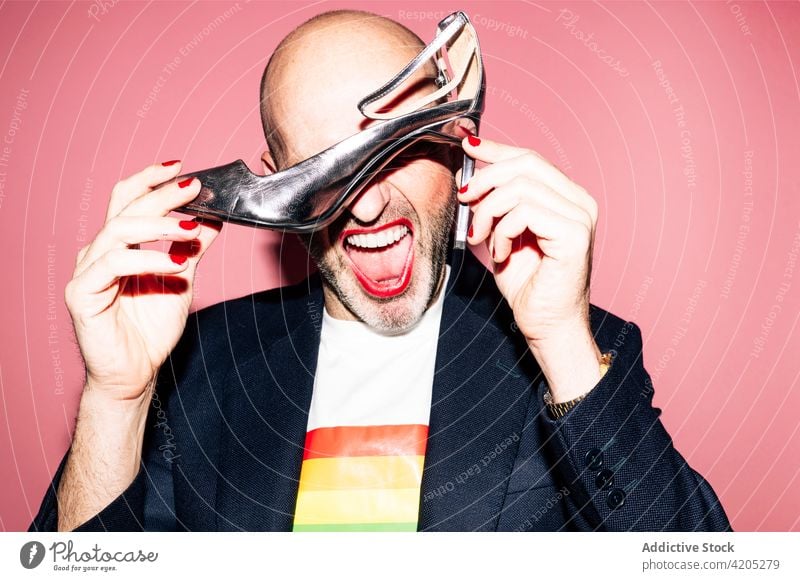 Expressive gay with makeup demonstrating high heeled shoe in studio man cover eyes lgbt homosexual eccentric concept alternative pride transsexual gender