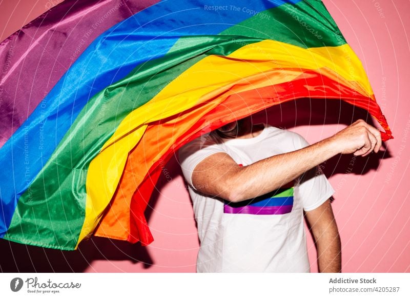 Happy man waving LGBT flag in pink studio homosexual lgbt happy gay makeup concept pride rainbow equal male unshaven red lips respect tolerance positive glad