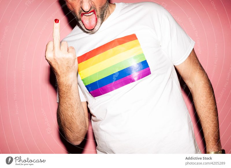 Anonymous homosexual man with makeup and beard showing middle finger fuck lgbt gay tongue out rebel pride flag concept naughty liberty rainbow male unshaven