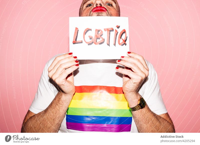 Positive gay showing paper with LGBTIQ inscription in pink studio man homosexual lgbtiq pride queer grimace concept demonstrate hide support activism male adult