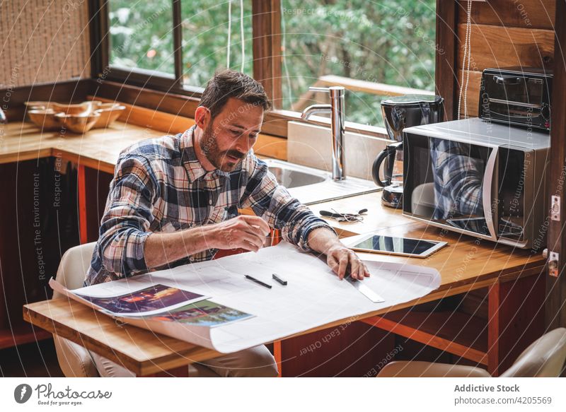 Busy man drawing draft of house at home architect blueprint sketch project building busy paper male plan sit table kitchen serious concentrate focus