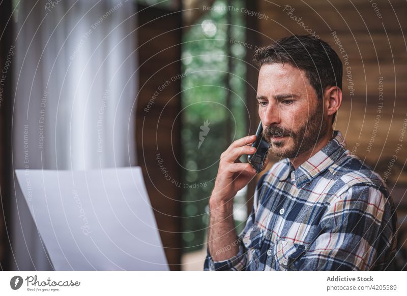 Serious male architect talking on smartphone during remote work blueprint man project sketch discuss speak busy paper plan home drawing serious concentrate
