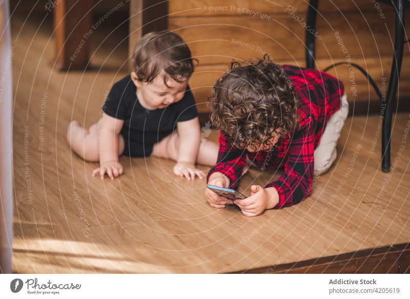 Cute siblings sitting on wooden floor in house children browsing smartphone little cute home entertain adorable boy brother gadget device kid using childhood