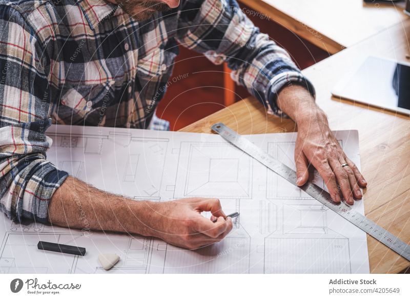 Anonymous man drawing draft of house at home architect blueprint sketch project building busy paper male plan sit table kitchen serious concentrate focus