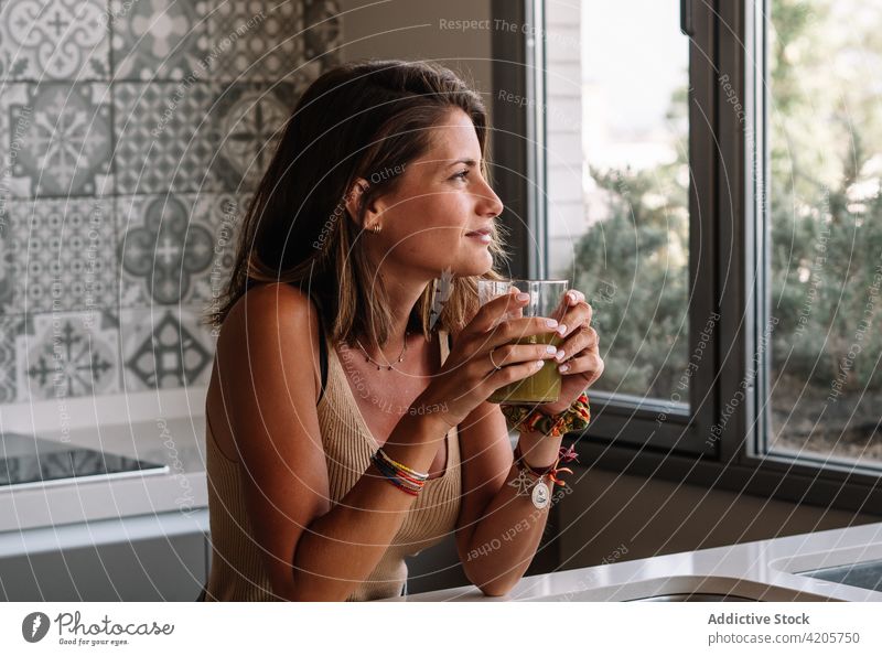 Caucasian girl is having a green vegetable juice in front of her big kitchen window. woman balanced shake layout tabletop celery freshly lettuce soft greenery