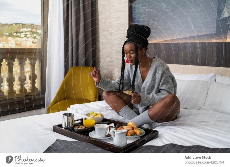 Happy young black lady having breakfast in cozy hotel room woman drink coffee bed content smile comfort tourist relax delicious female african american ethnic