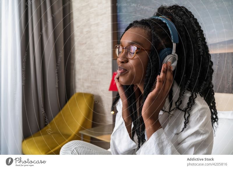 Smiling young black woman using mobile phone and listening to music with headphones smile online positive internet connection communicate female smartphone