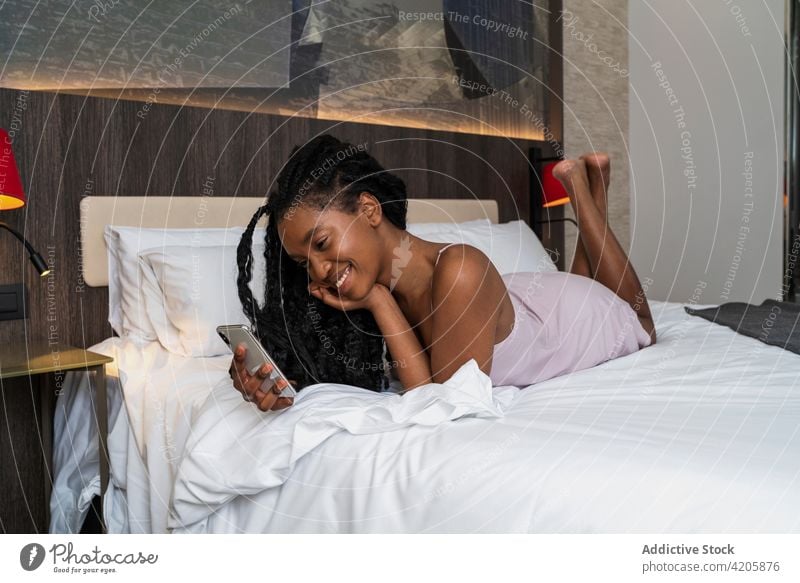 Cheerful young black lady using smartphone on cozy bed woman happy smile relax allure message social media online cheerful lying female african american ethnic