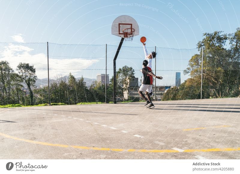 Black man and hispanic friend playing streetball on sports ground player together men basketball hoop score multiethnic playground jump male black
