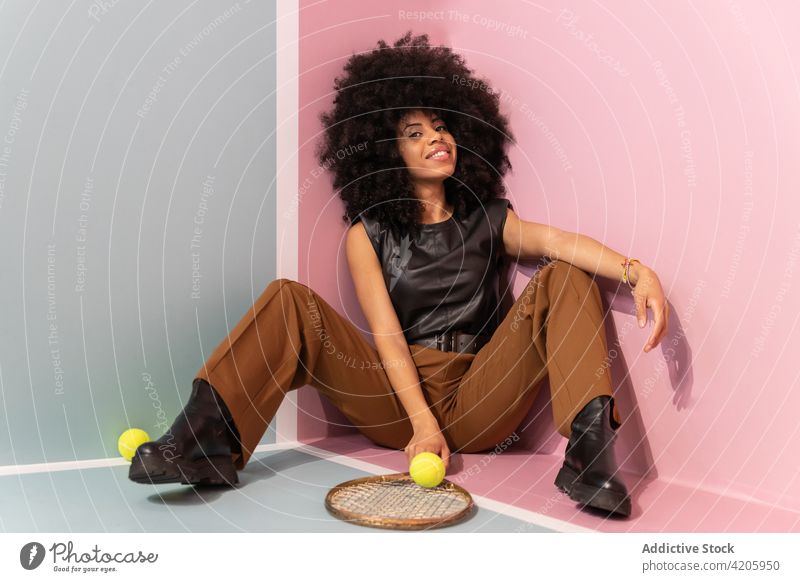 Black woman with tennis racket sitting in studio player court posture fashion trendy style female afro confident personality individuality appearance hobby