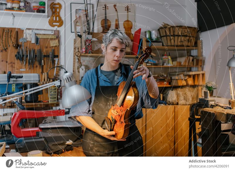 Female artisan examining violin in workshop craftswoman examine finish handmade professional shabby female apron workbench shelf storage studio production