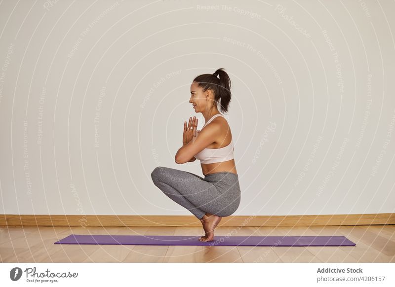 Content woman performing Squatting Toe Balance pose in room namaste yoga squatting toe balance smile practice wellness vitality energy content glad tiptoe