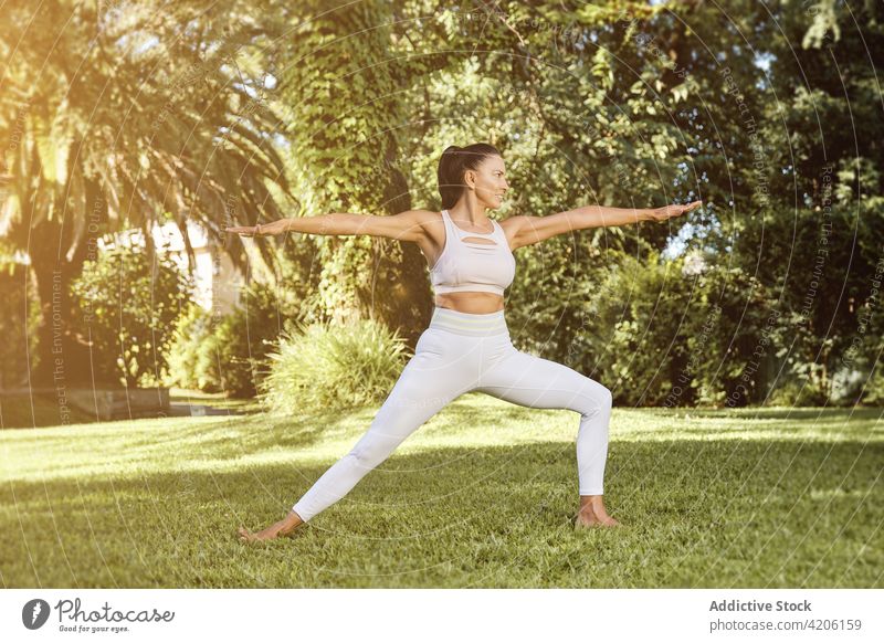 Woman showing Warrior two pose in park woman yoga balance practice smile stretch flexible wellbeing happy vitality healthy lifestyle energy Virabhadrasana two