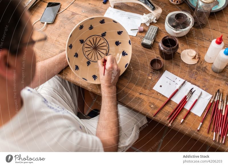Crop artist drawing on ceramic plate man brush craft workshop handmade hobby male paint design talent artisan professional create handicraft earthenware