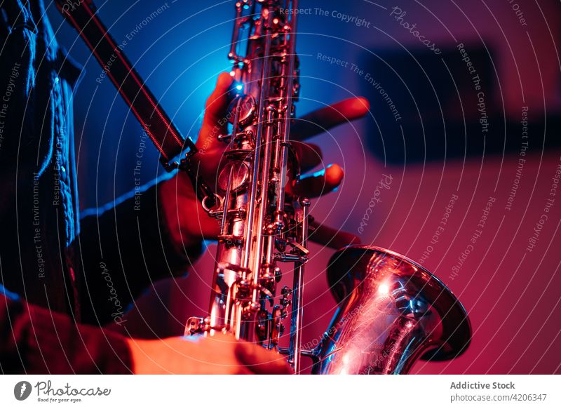 Crop unrecognizable musician playing saxophone at concert perform live key instrumental melody jazz sound professional club song entertain neon blue red person