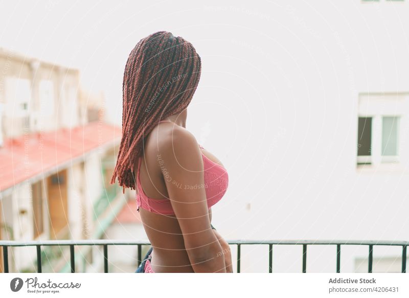 Black woman with braids standing on balcony hairstyle observe street lingerie underwear terrace female ethnic black african american pink hairdo body shape