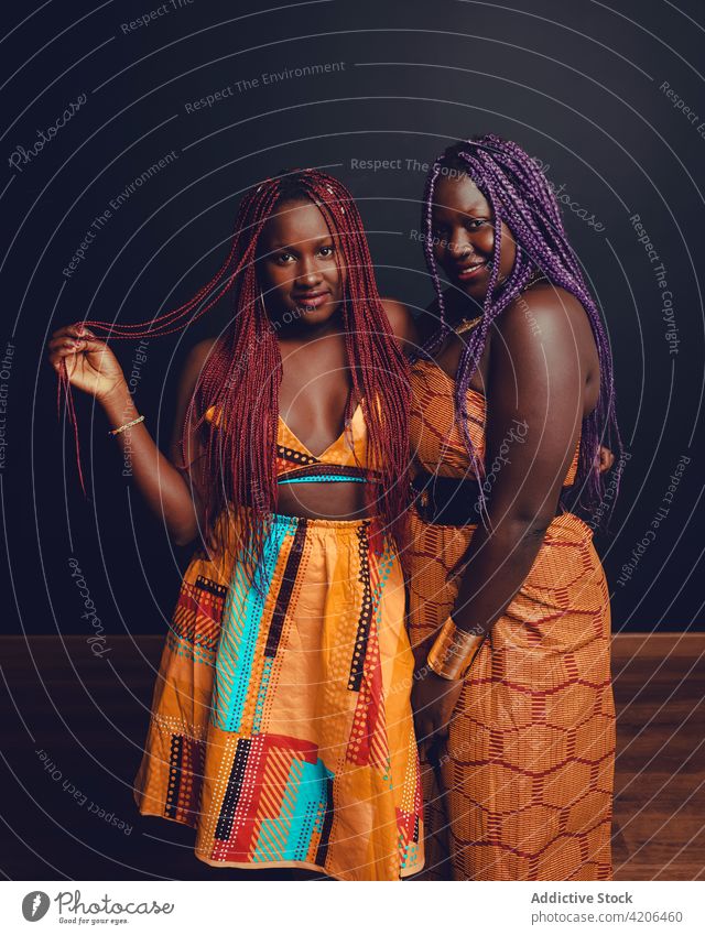 Smiling black women in traditional outfits standing in studio braid hairstyle bright friend long hair appearance female ethnic african american dark orange