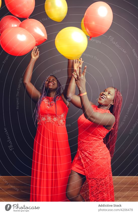 Carefree black women throwing balloons in air in studio celebrate air balloon festive cheerful having fun holiday event female ethnic african american toss