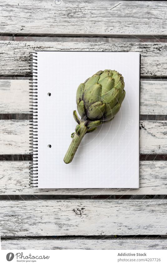 A artichoke on blank notebook on table herb fresh greenery notepad healthy food sprig desk paper page wooden natural minimal organic simple tasty delicious