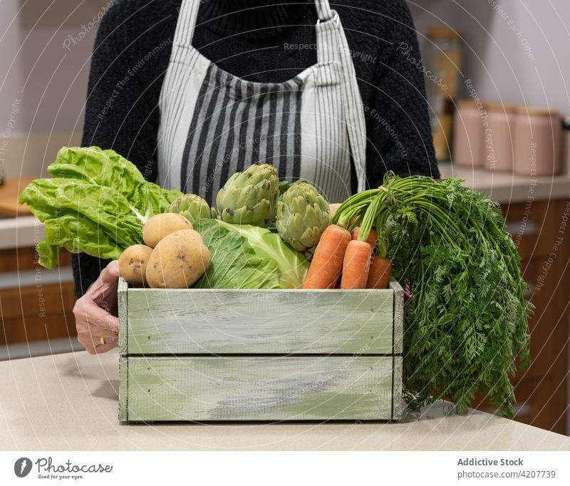 Crop elderly woman with vegetables in wooden box grocery harvest fresh ripe assorted natural senior female food apron kitchen product organic potato carrot