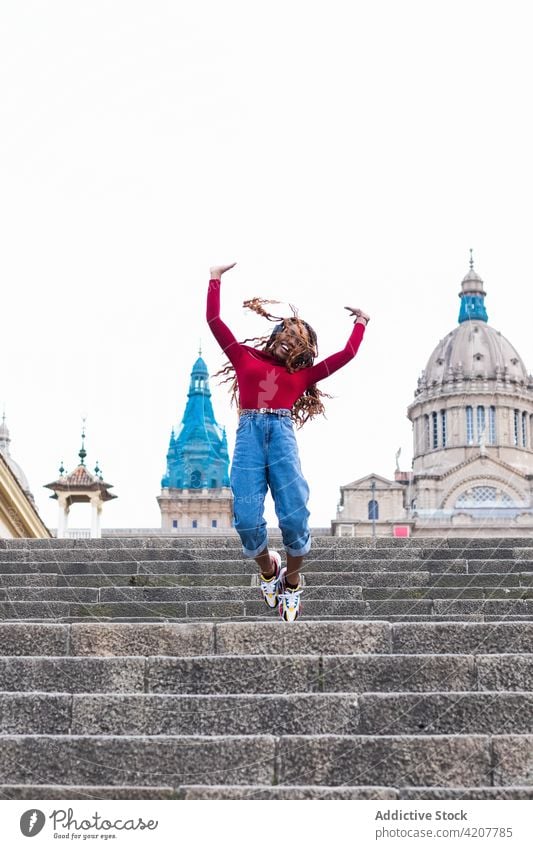 Cheerful black woman jumping on stairs in city moment listen music carefree cheerful rock gesture female ethnic african american headphones smile glad
