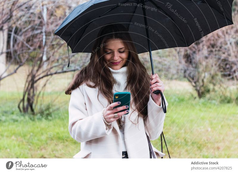 Woman with umbrella using smartphone on street woman style rain mobile spring fashion coat female adult gadget device lifestyle browsing stroll surfing