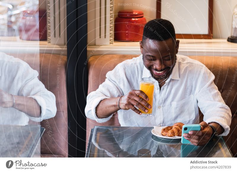 Cheerful black man using smartphone in cafe happy mobile juice breakfast browsing adult male african american ethnic gadget device surfing internet lifestyle