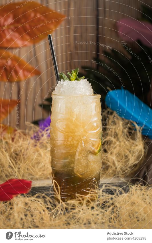 Tiki glass of tropical cocktail with ice tiki mug beverage alcohol drink booze dry grass leaf colorful straw herb refreshment liquor glassware cloth fabric