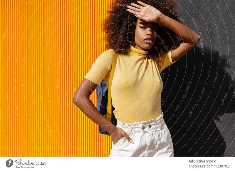 Trendy black woman standing on yellow and black background afro hairstyle colorful portrait bright african american ethnic trendy charismatic curly hair casual