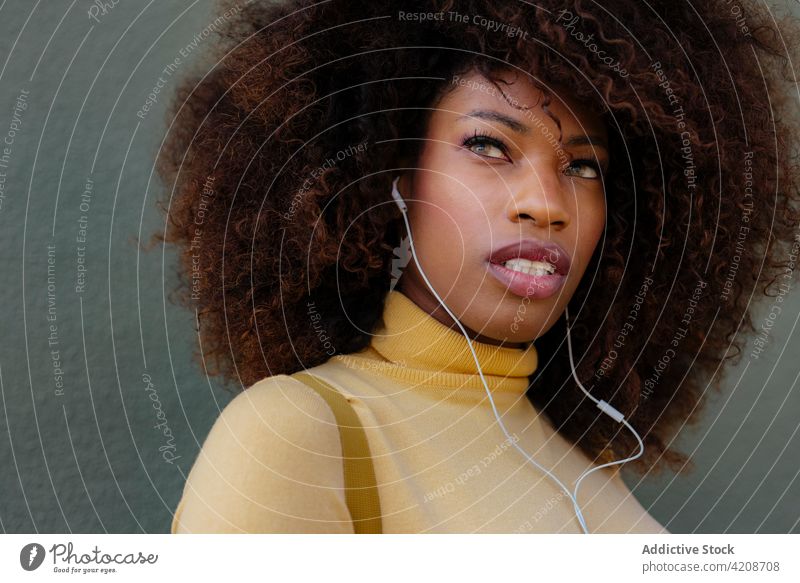 Dreamy black woman listening to music in earphones dreamy spare time sincere afro portrait using device song hairstyle charming wistful pensive wire audio