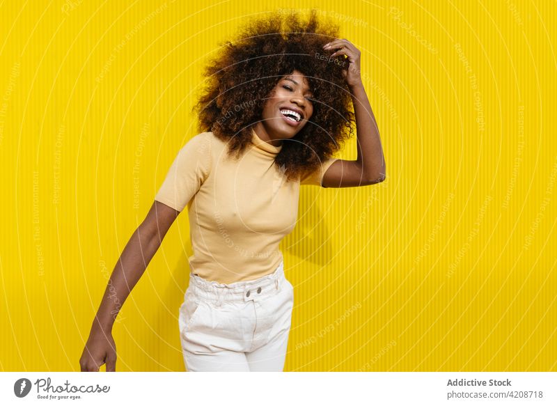 Glad trendy black woman laughing on yellow background cheerful touch hair afro hairstyle charming enjoy candid colorful portrait glad content happy bright smile