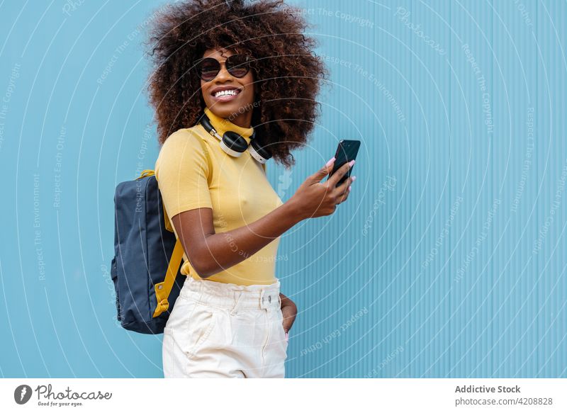 Cheerful black woman taking selfie on smartphone in sunlight browsing memory moment content headphones portrait using gadget free time colorful device