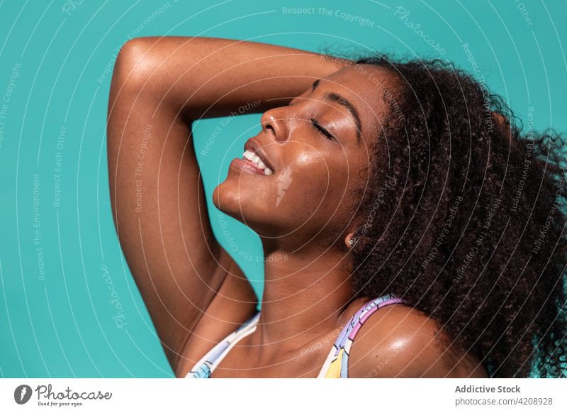 Crop of gorgeous black woman in swimwear on blue background swimsuit style toothy smile eyes closed happy cheerful feminine touch hair cool outfit carefree