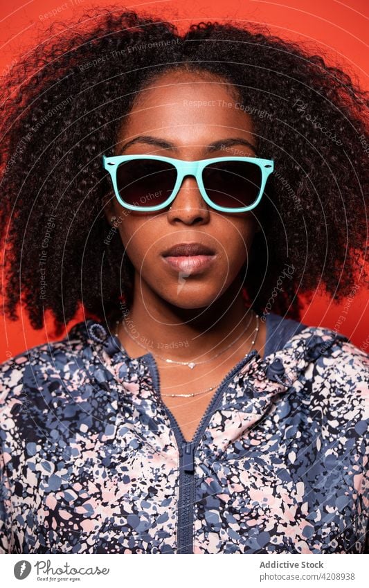 Stylish black woman in sunglasses against red background confident style cool outfit appearance independent calm trendy street style accessory serious apparel