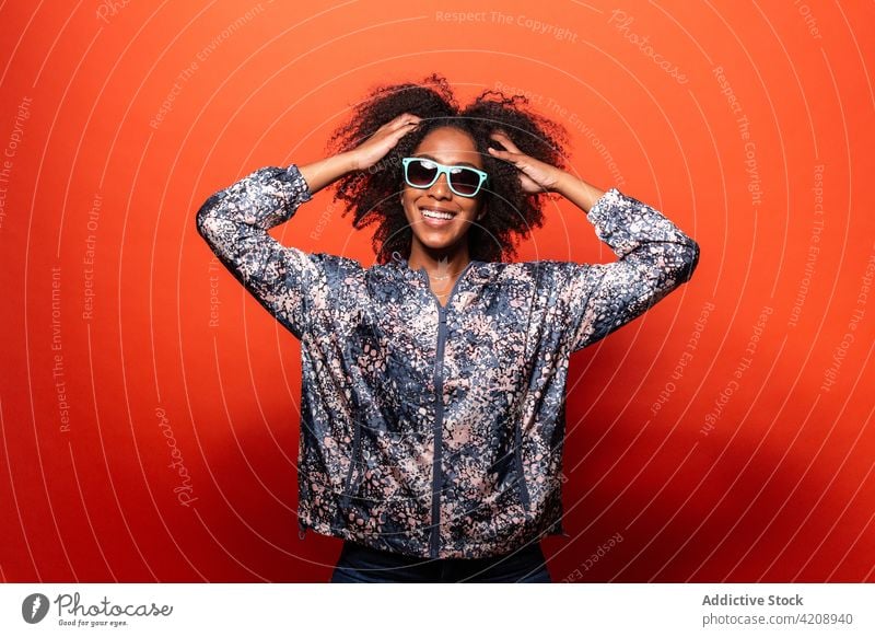 Stylish black woman in sunglasses against red background confident style cool outfit appearance independent happy calm trendy smile street style accessory