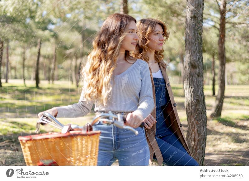 Cheerful women smiling on bicycle in park cheerful girlfriend nature happy optimist female summer sunny together young positive free time delight weekend