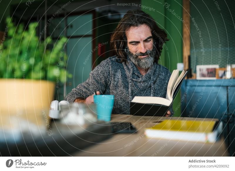 Mature ethnic man reading book in house literature knowledge smile interested free time hot drink home table hispanic beverage textbook spare time cup weekend