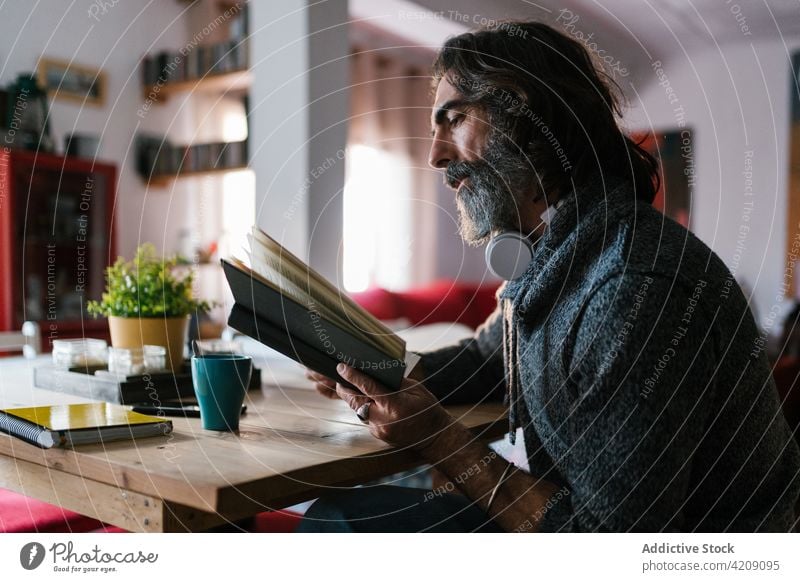Mature Hispanic man reading book in house room textbook literature wisdom knowledge pastime weekend portrait interested home education table headset hispanic