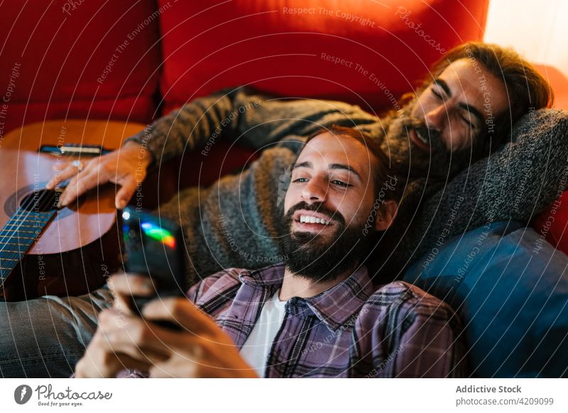 Content Hispanic father with son sharing smartphone on sofa share spend time weekend smile portrait using gadget men device together enjoy cellphone internet