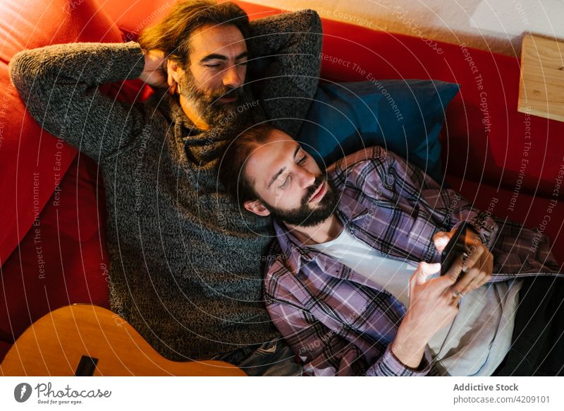 Hispanic father with son sharing smartphone on sofa share spend time weekend smile portrait using gadget men device together enjoy cellphone internet online