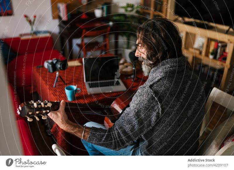 Hispanic guitarist playing guitar while watching video on laptop lesson study learn man using gadget device screen knowledge musician acoustic art sit home