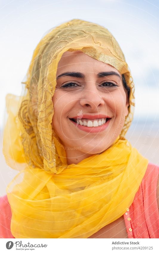 Cheerful woman in bright yellow headscarf smiling cheerful smile pleasant nature portrait environment appearance female young feminine silk cloudy sky gray lady