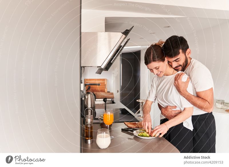 Loving young multiracial couple embracing in kitchen before breakfast hug avocado smile love romantic together relationship happy healthy affection close