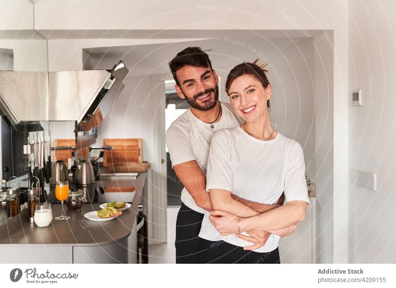 Loving young multiracial couple embracing in kitchen before breakfast hug avocado smile love romantic together relationship happy healthy affection close