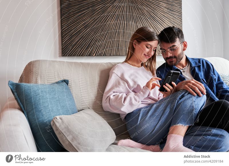 Positive young multiracial couple sharing smartphone on couch using sofa positive romantic together relationship rest love weekend home share boyfriend