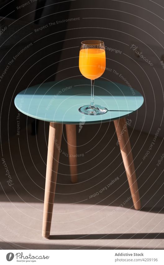 Glass of fresh juice placed on small table in modern apartment orange glass healthy natural detox drink design tasty organic sunlight sofa style home beverage