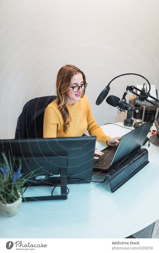 Cheerful woman working on laptop at radio station broadcast studio microphone equipment device browsing surfing special modern netbook table female positive